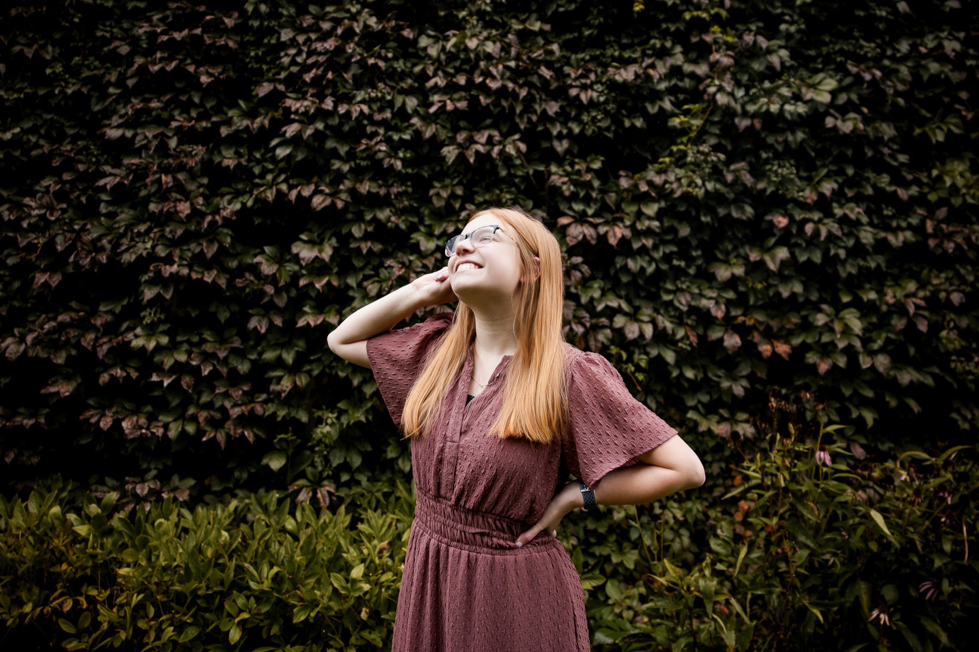 Hannah in a rose dress looking up in front of an ivy wall