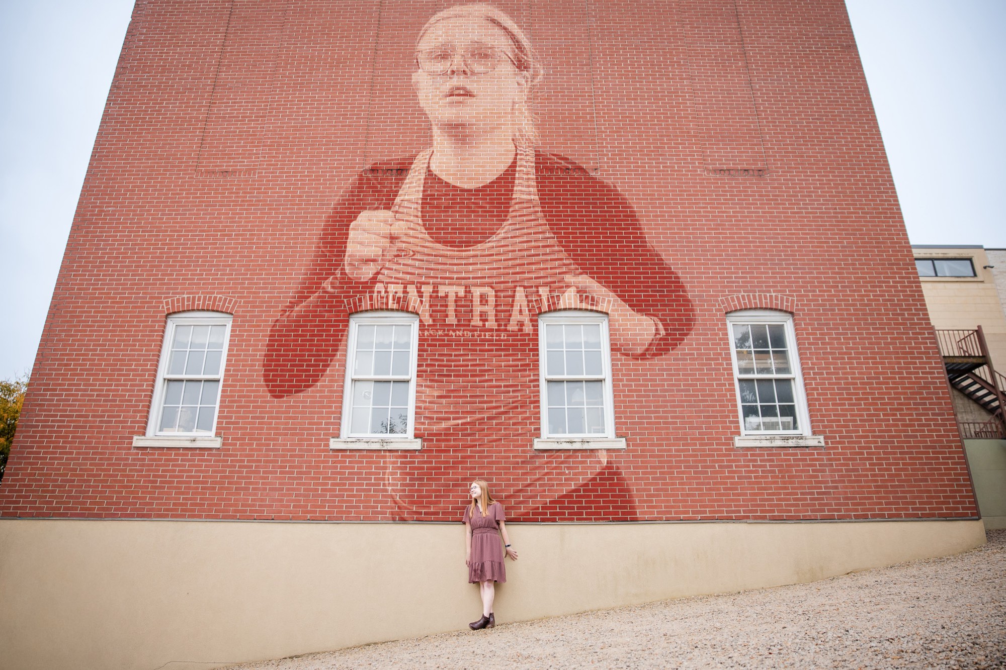 Hannah standing beneath the giant Central mural on a brick wall
