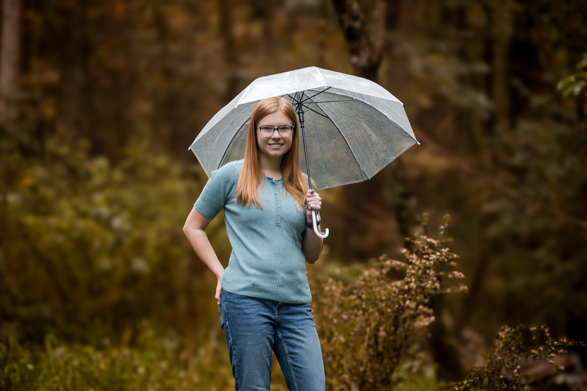Hannah holding a clear umbrella in the autumn woods