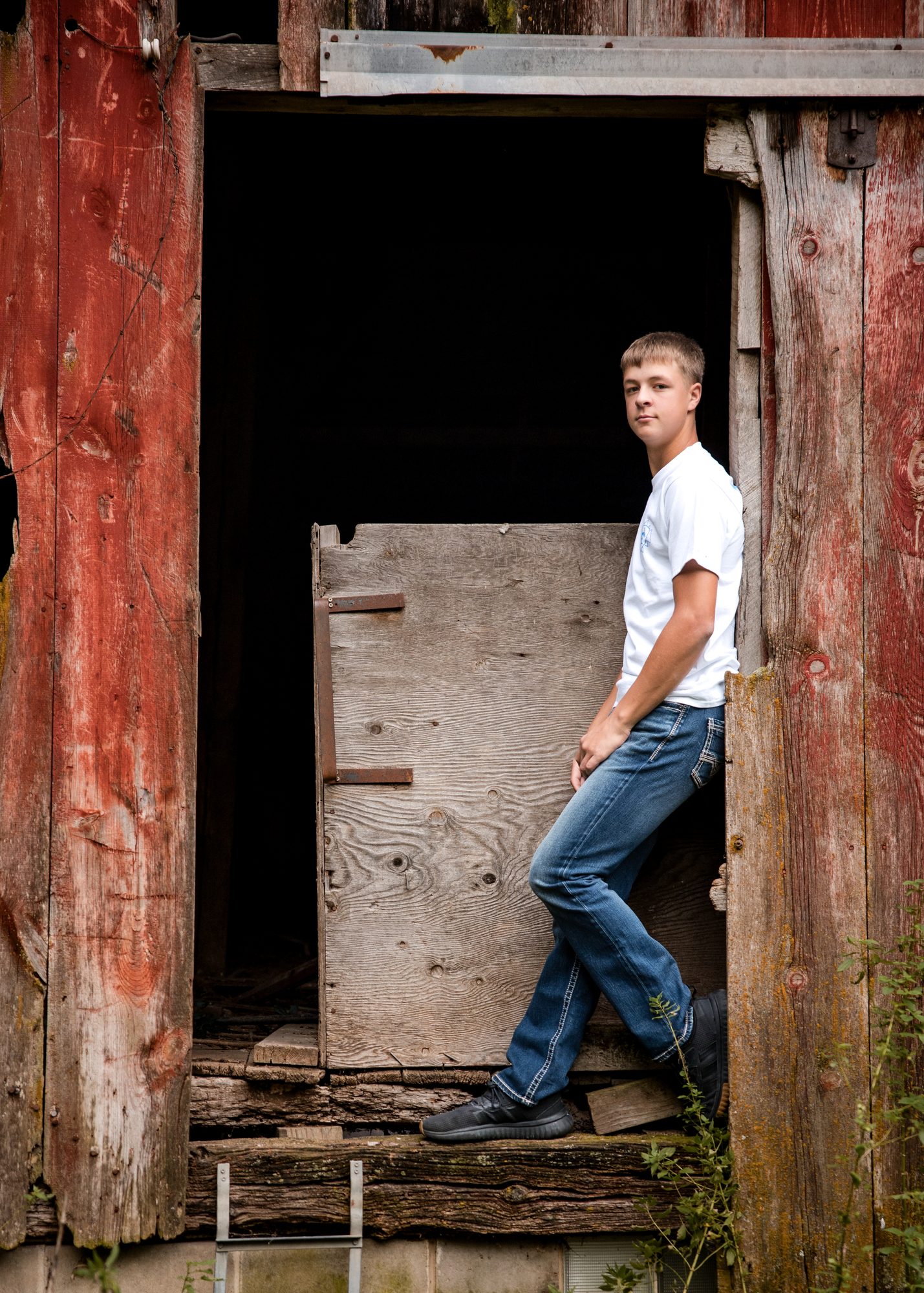 Jaxon leaning in the doorway of a weathered red barn
