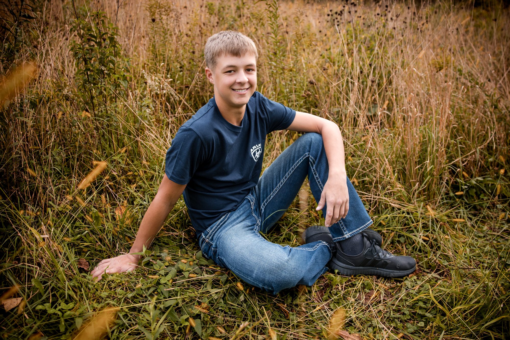 Jaxon sitting in tall autumn grass in a navy T-shirt