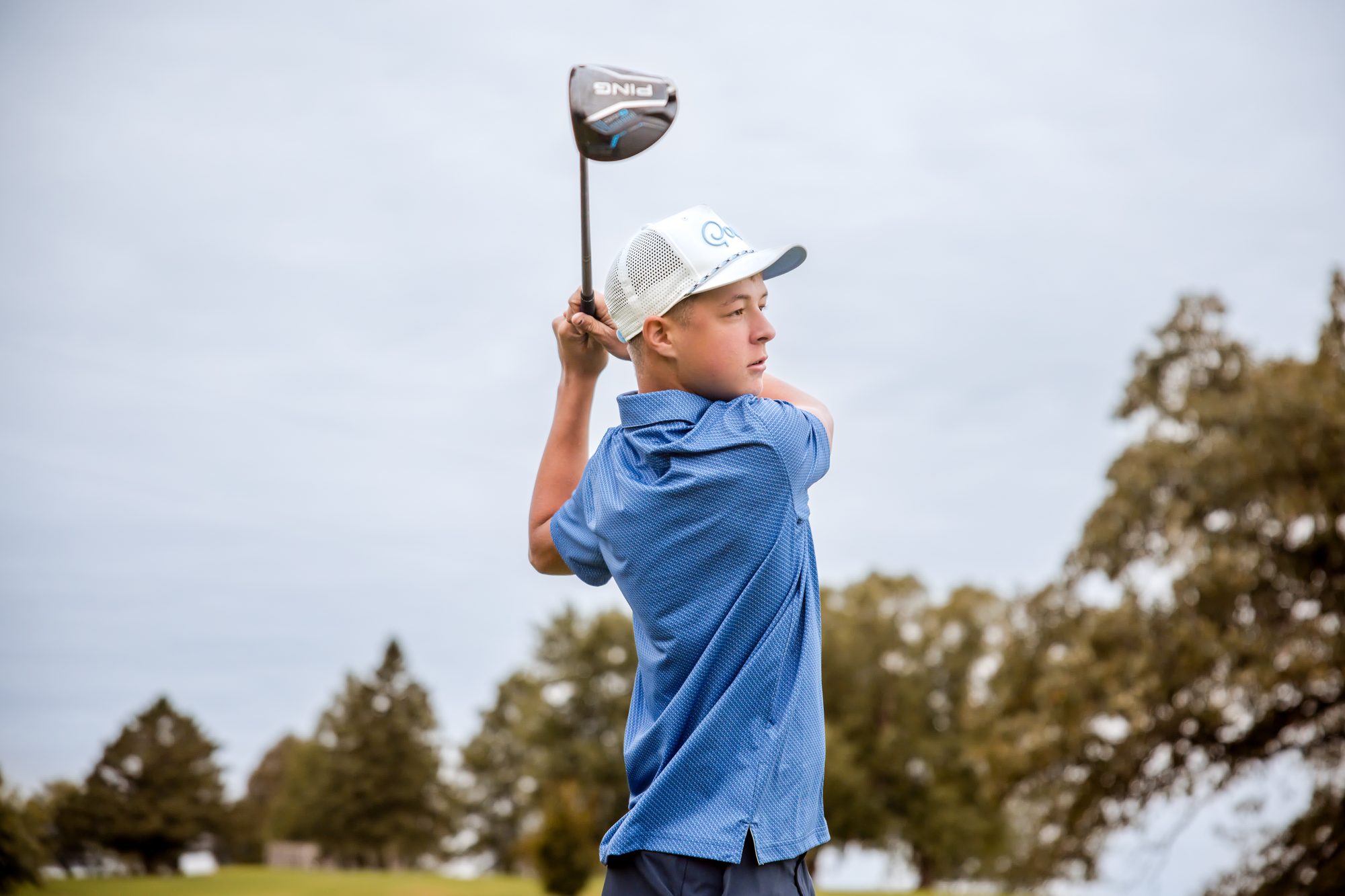 Jaxon finishing a golf swing under a cloudy sky