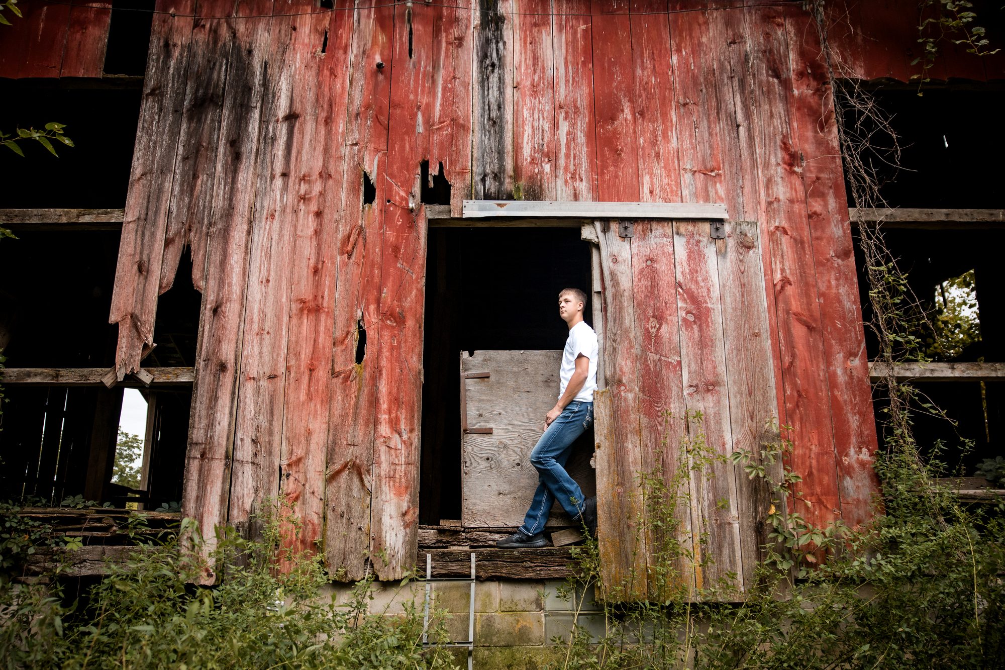 Jaxon standing in the open door of a tall weathered red barn on the farm