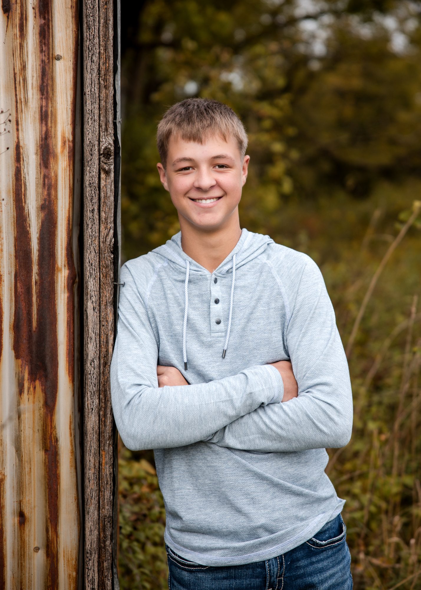 Jaxon smiling with his arms crossed against an old wooden shed