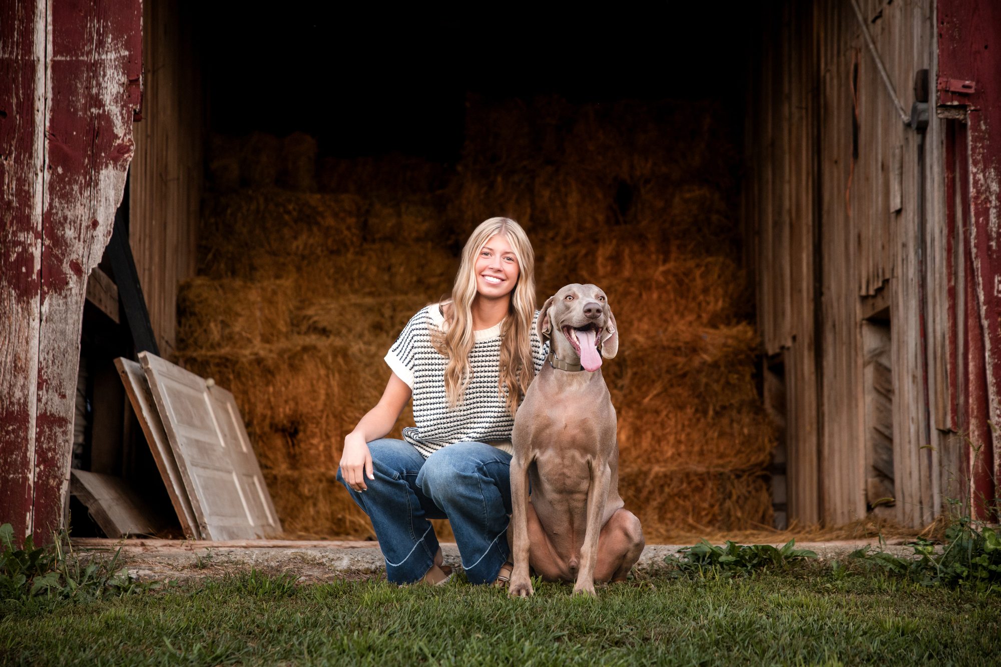 Katie kneeling with her dog in front of a hay-filled barn