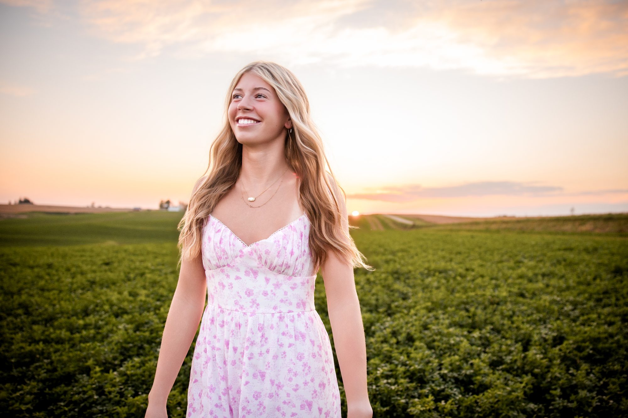 Katie in a floral dress in an alfalfa field at sunset