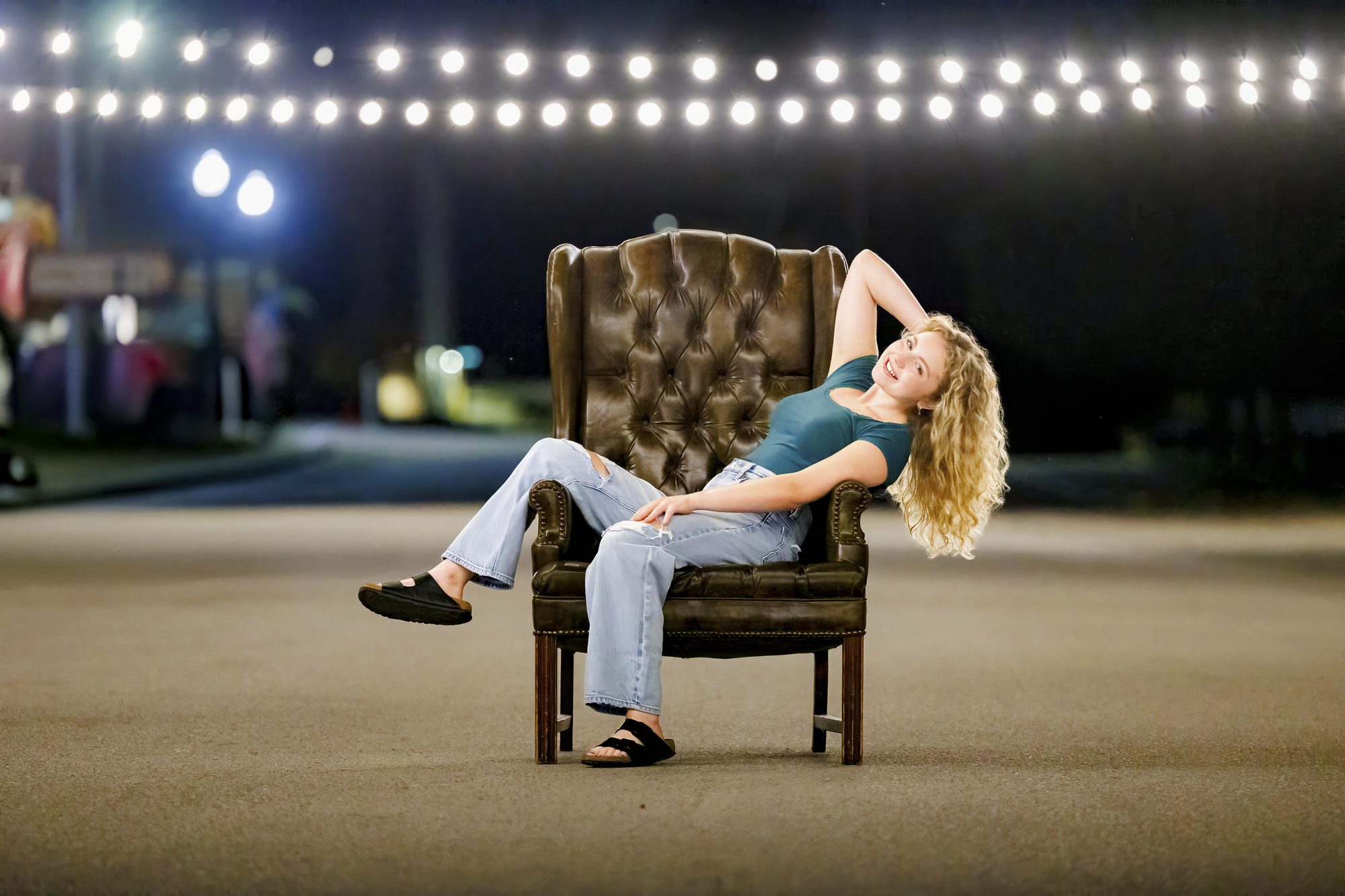 Teagan lounging in a leather wingback chair under string lights at night