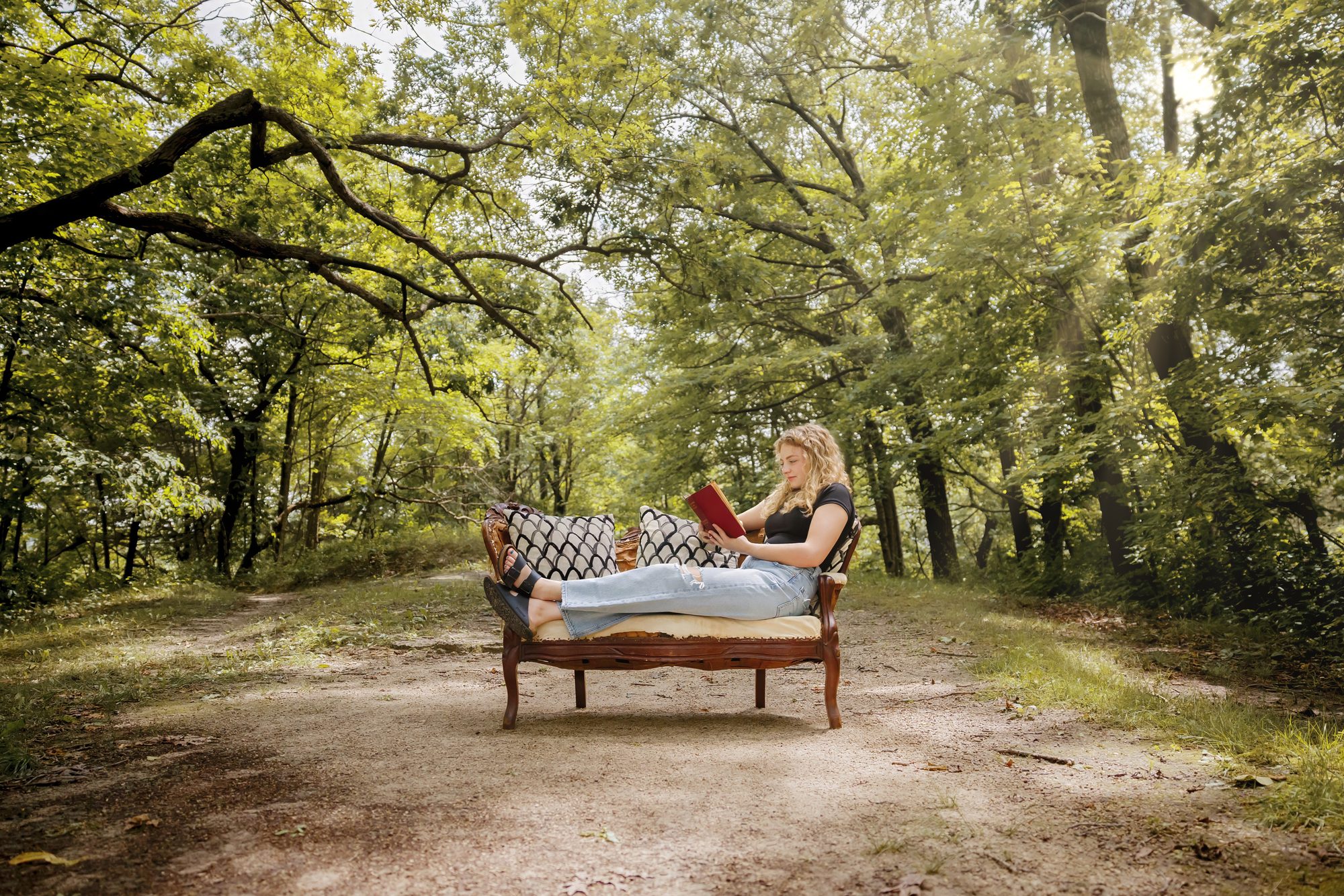Teagan reading on a vintage couch on a tree-lined path