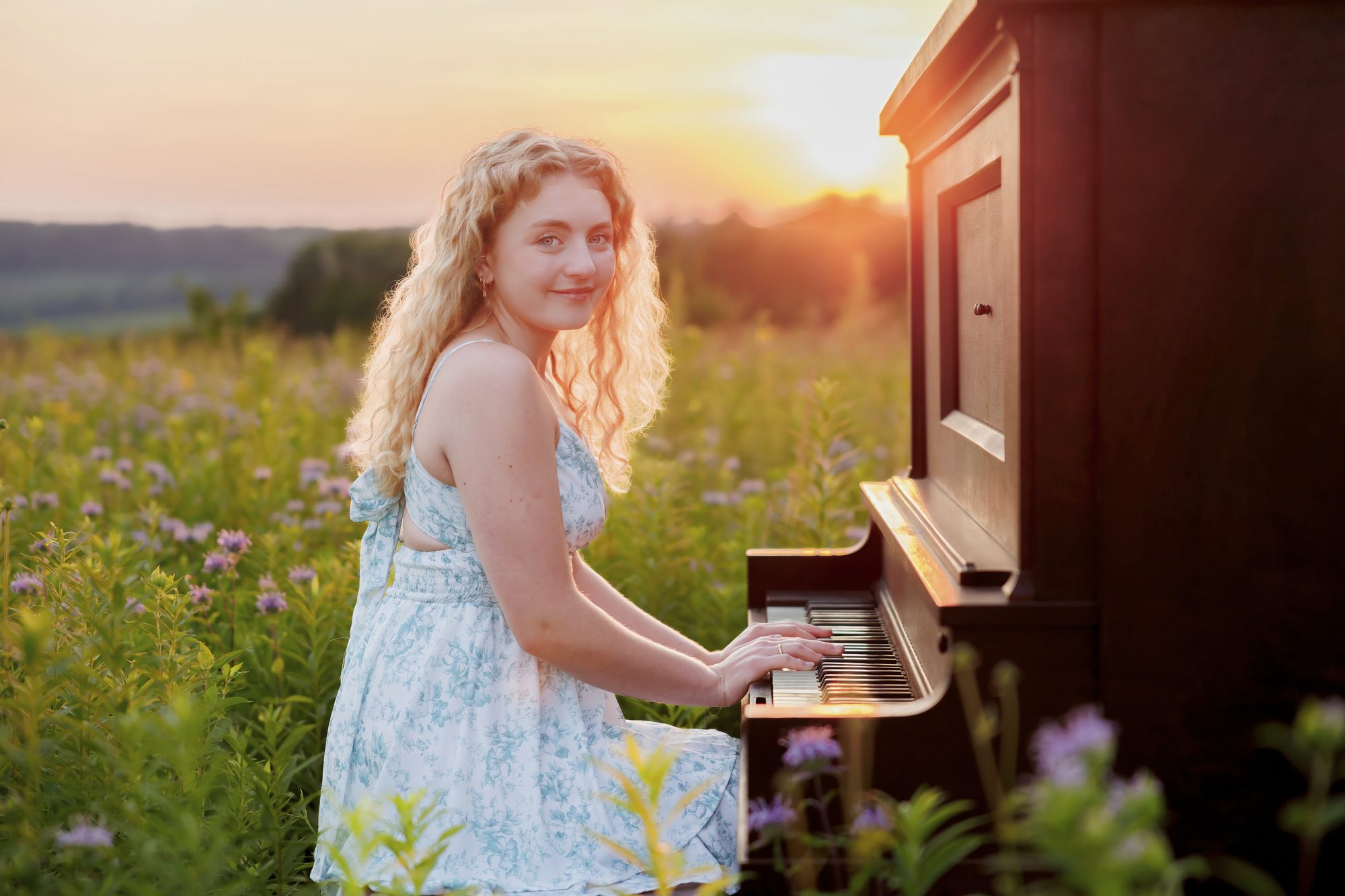 Teagan playing an upright piano in a wildflower field at sunset