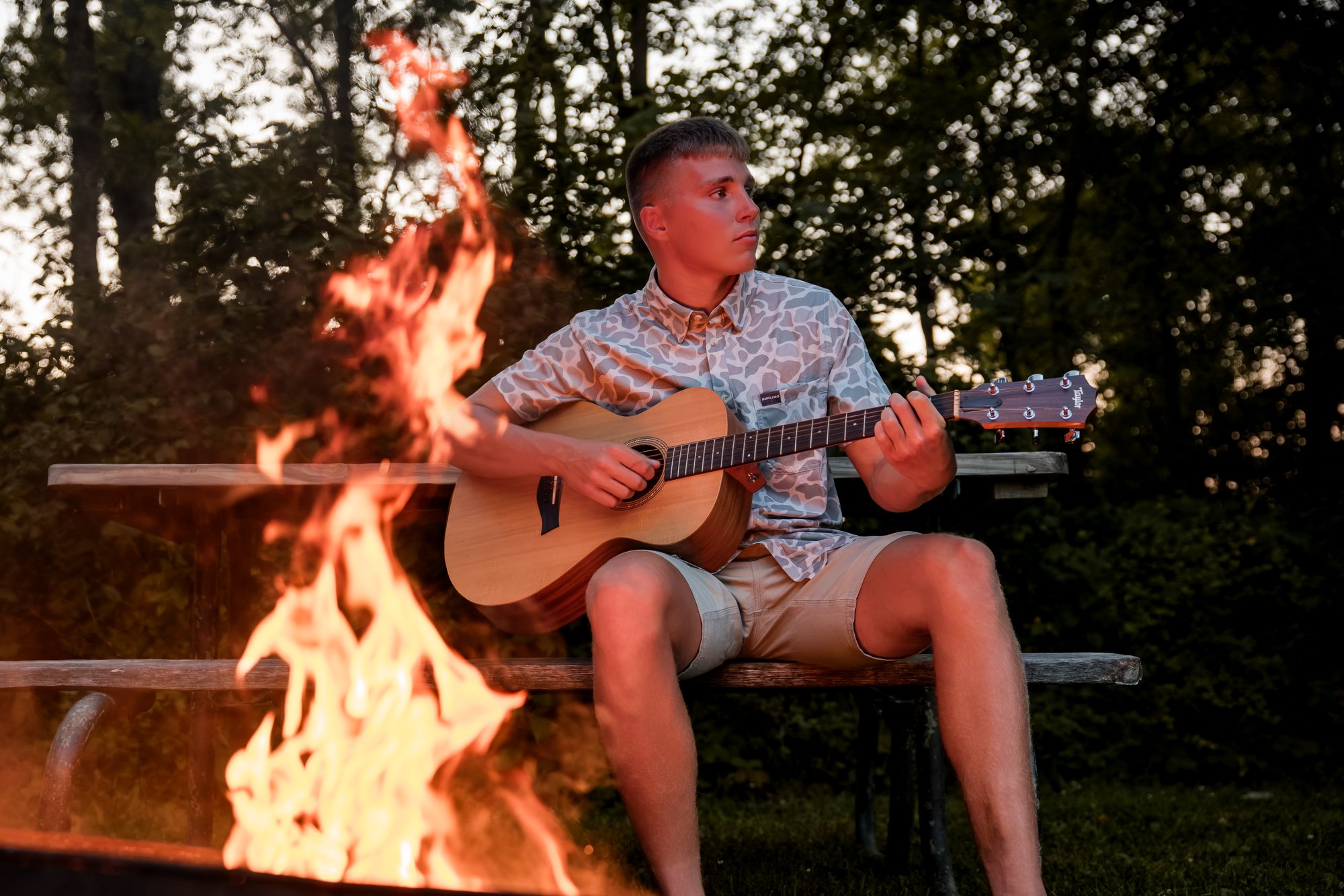 Jax Tommasin playing guitar beside a fire at dusk