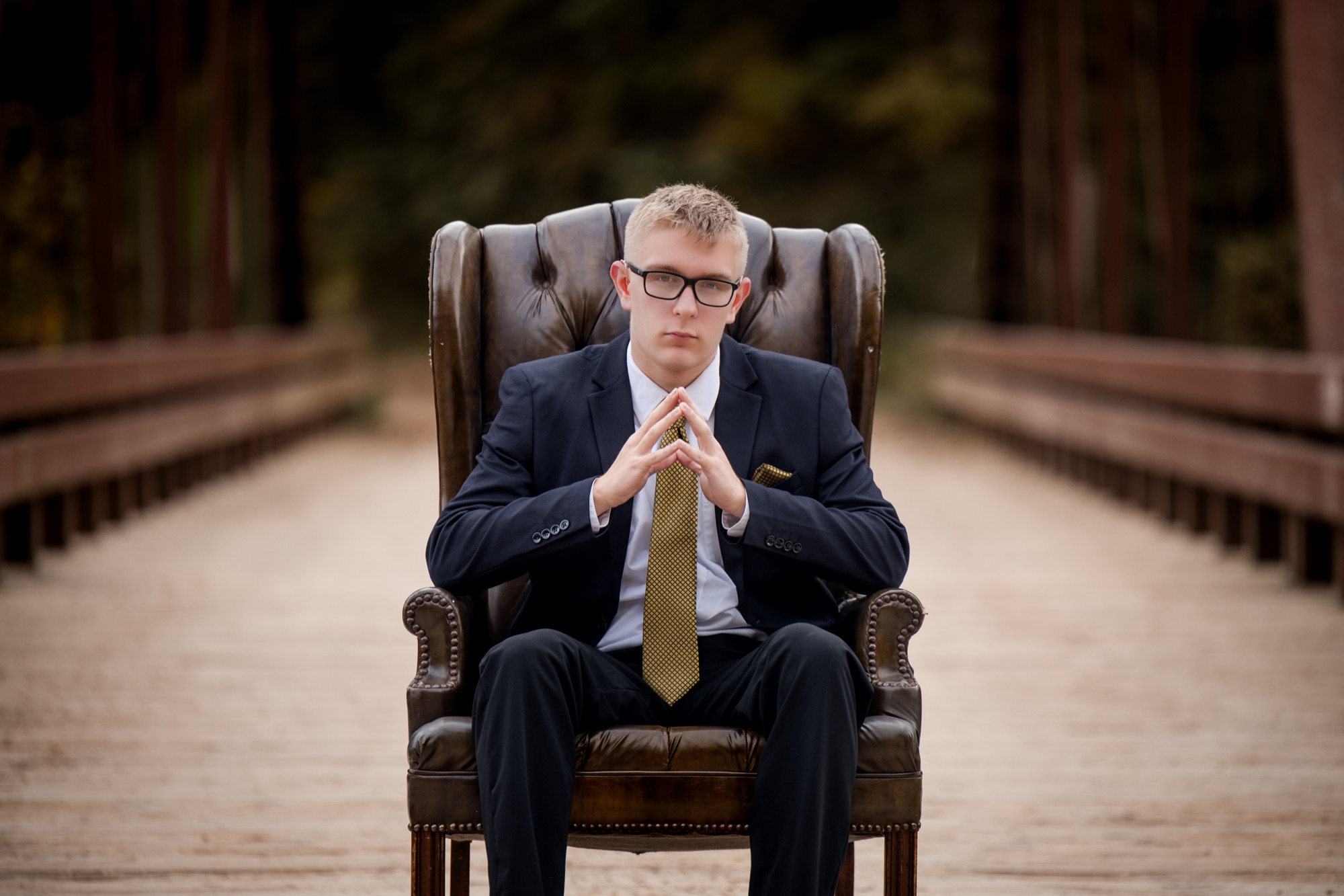 Tucker in a navy suit seated in a leather wingback chair on a wooden bridge