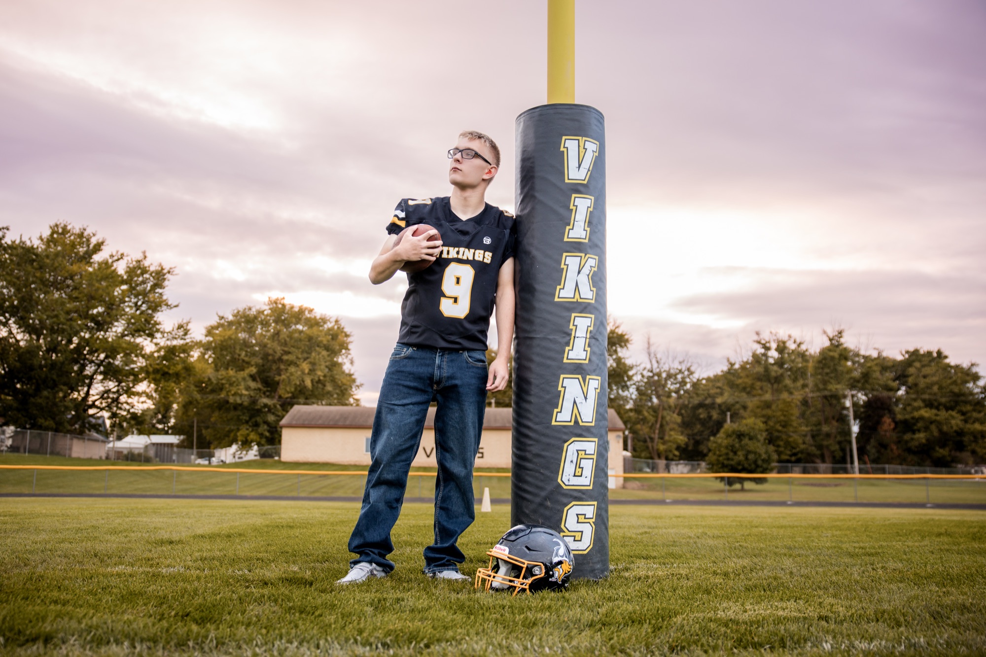 Tucker in his number 9 Vikings jersey beside the padded goal post, football and helmet in hand